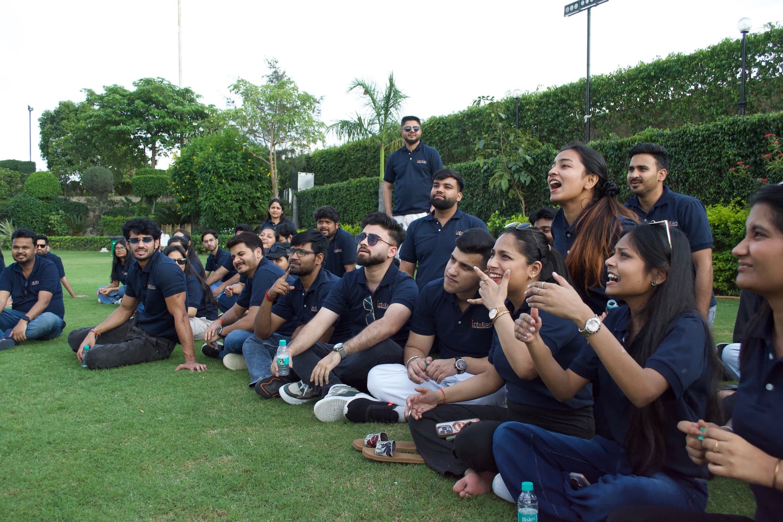 The Infollion team in matching polos, sitting on a lawn and cheering during an offsite activity.